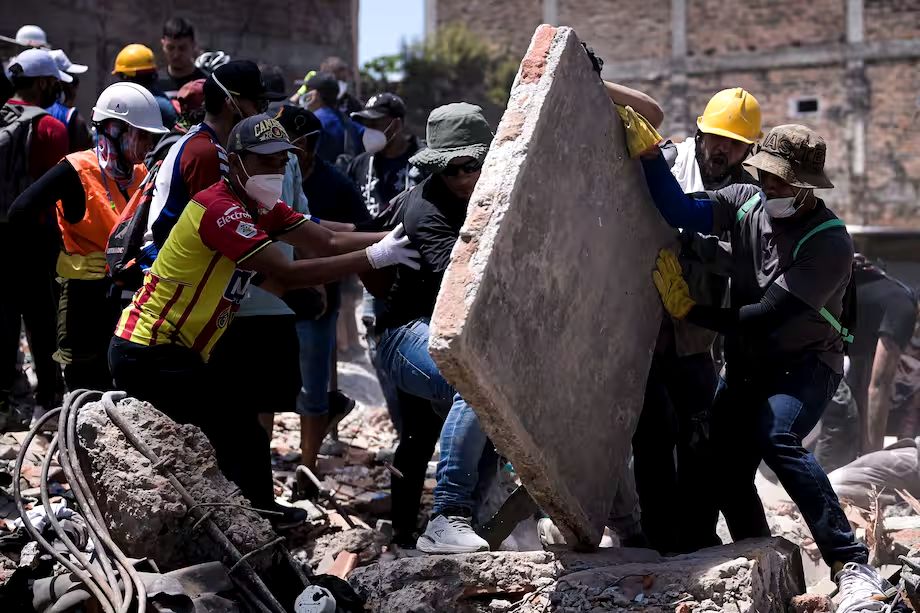 Un grupo de personas levanta entre todos una losa de concreto sobre los escombros